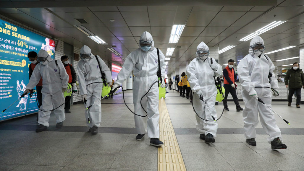 Five men in hazmat suits spray disinfectant on the floor of a subway in Korea