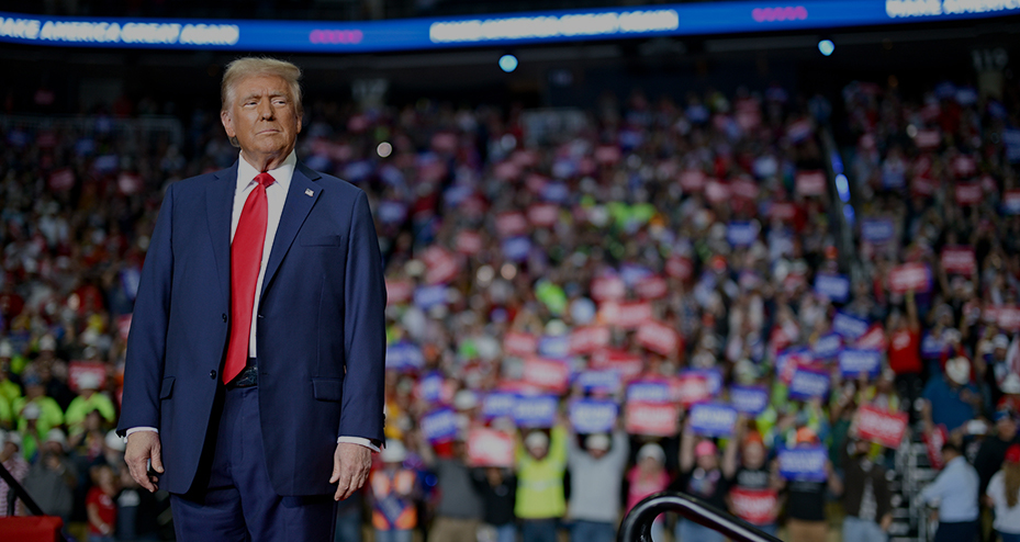 Donald Trump on stage with a large crowd of supporters seated in stands behind him