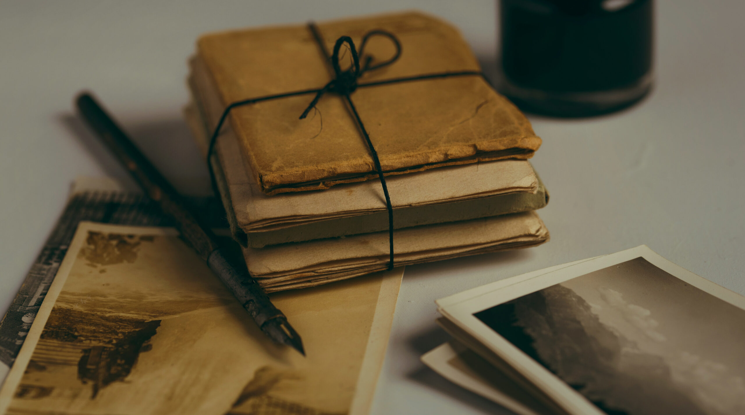 Old, well-worn canvas notebook on top of old photographs and a fountain pen